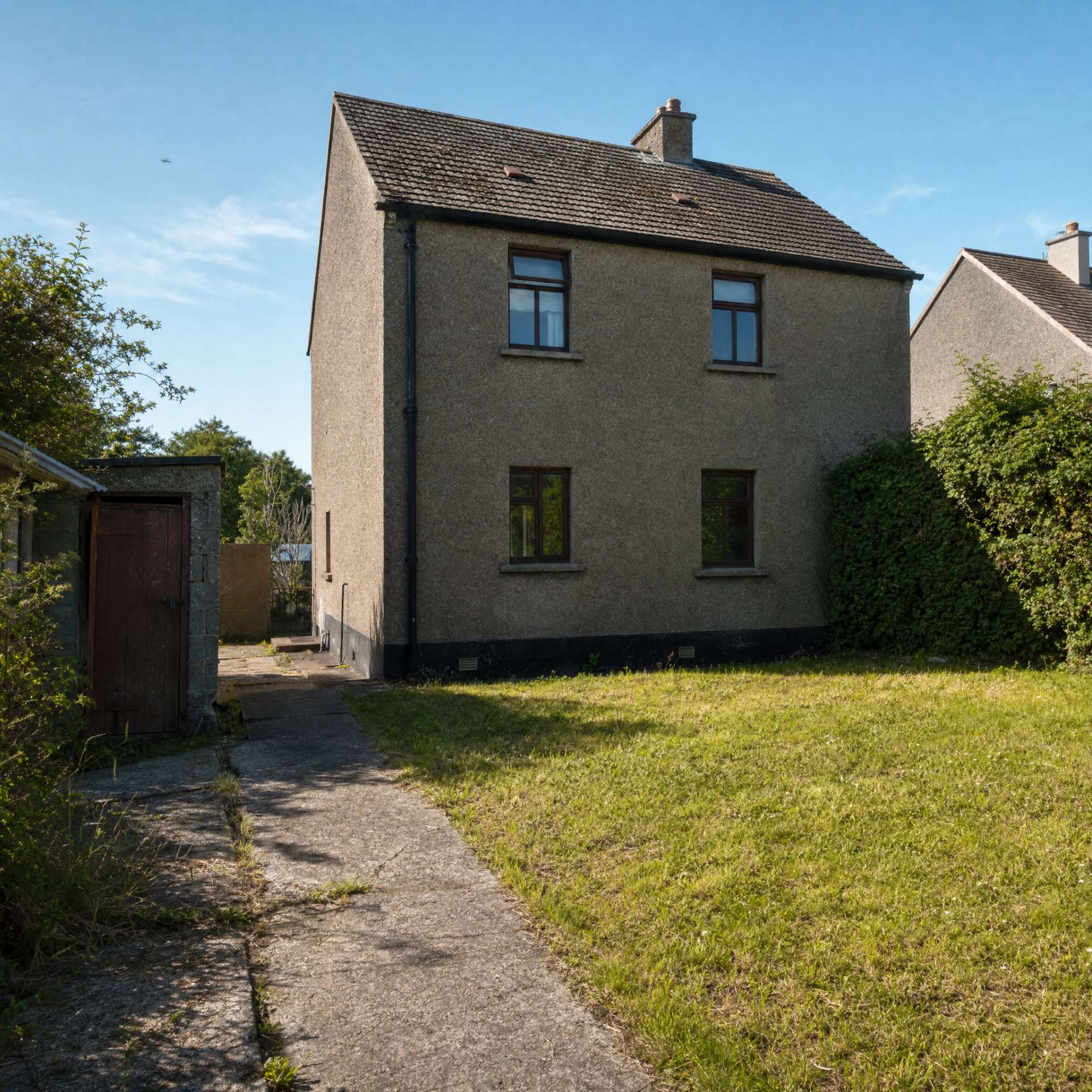 The rear of a dated house before its extension — a plain back wall, an old stone shed and a rough lawn.