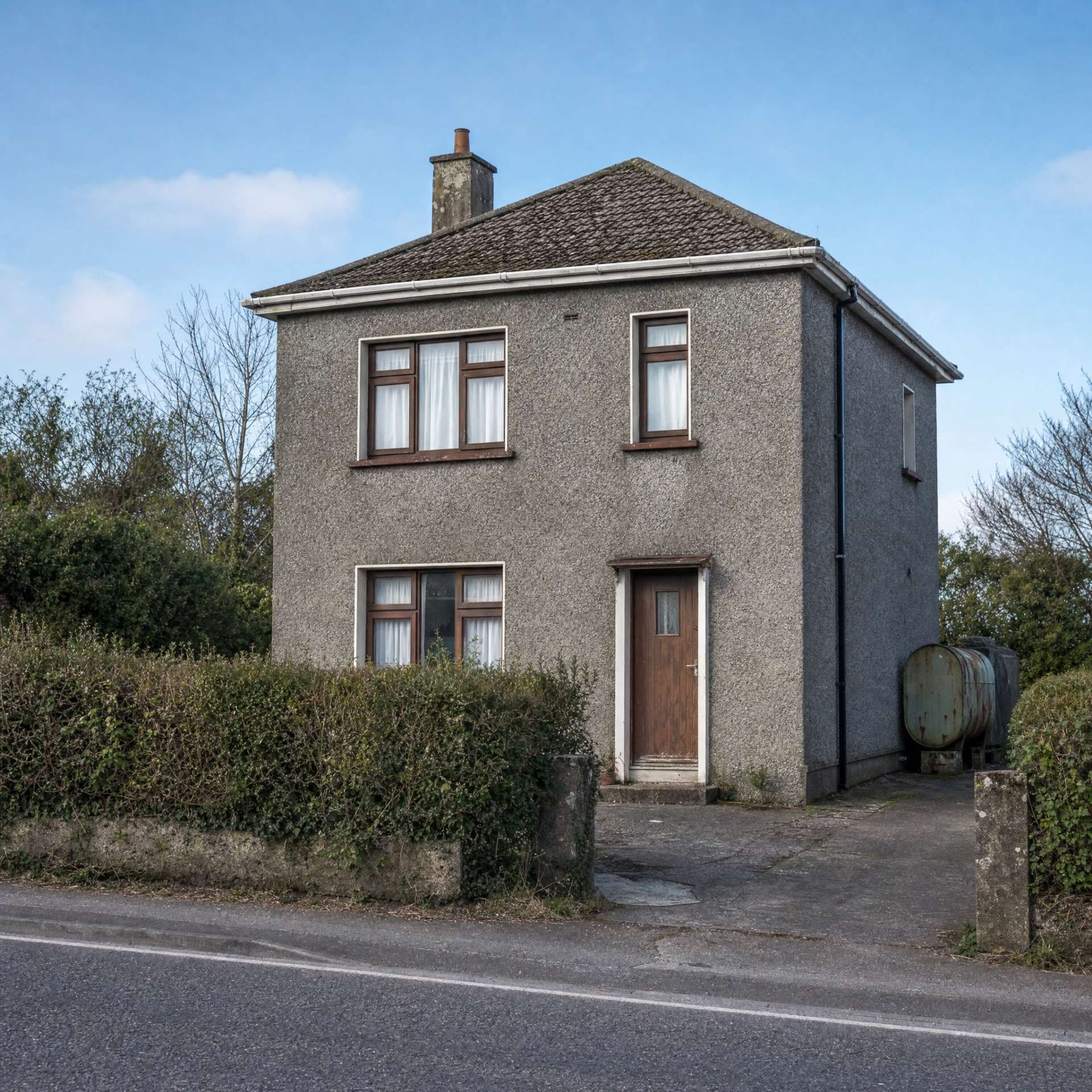 A cold pebble-dash house before retrofit — old timber windows, a mossy roof and a rusting oil tank at the side.