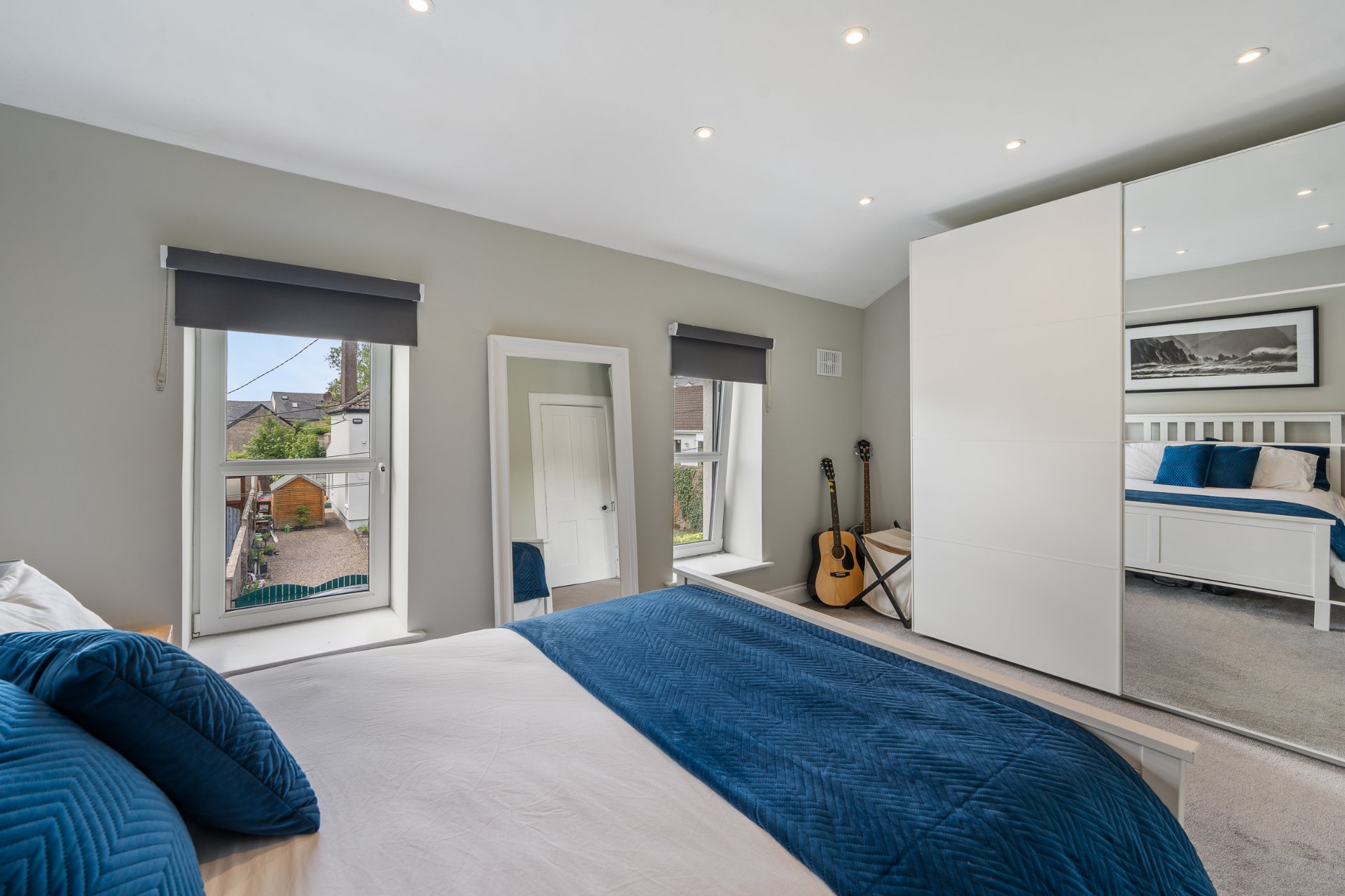 The main bedroom after renovation — soft grey walls, a mirrored wardrobe and a garden view.