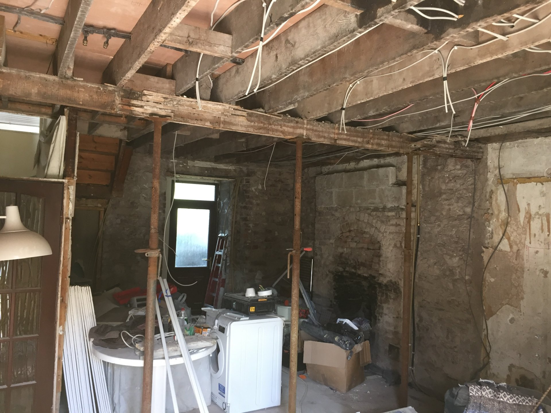 The interior stripped out — bare stone walls, exposed joists and steel props, with the old fireplace opened up.