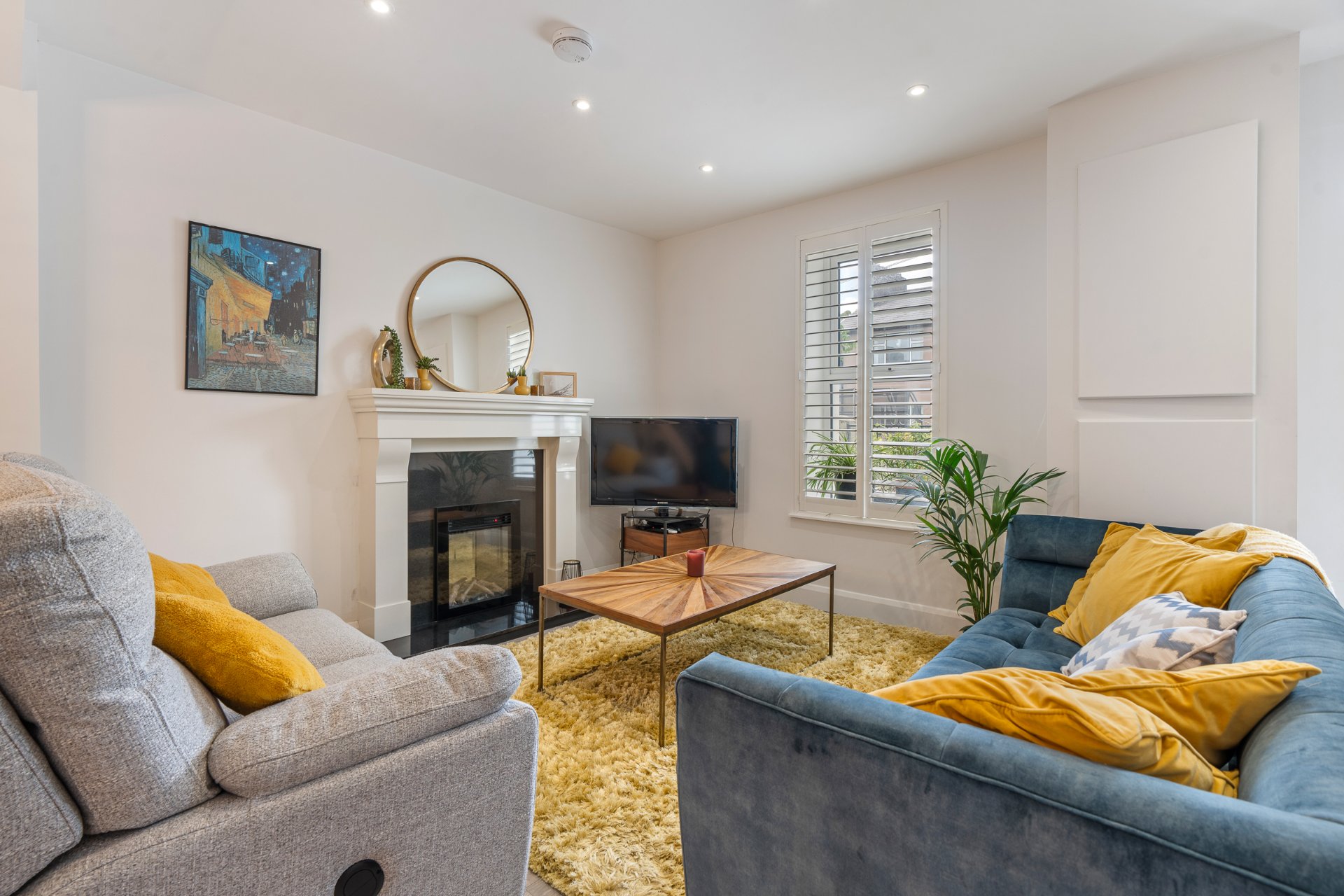 The living room with a restored fireplace, shutters and a warm modern scheme.