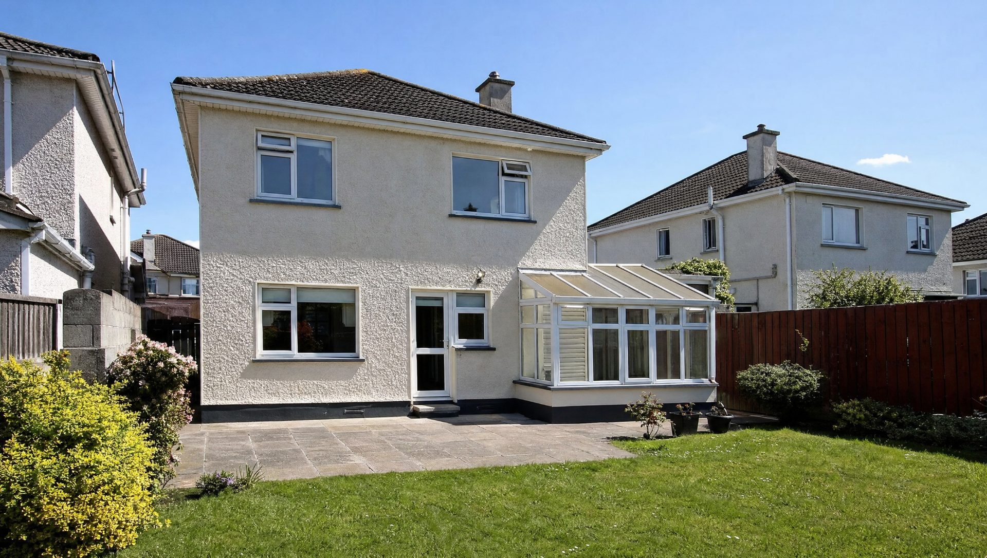 The same house before — a dated white uPVC lean-to conservatory on the rear and older patio paving.