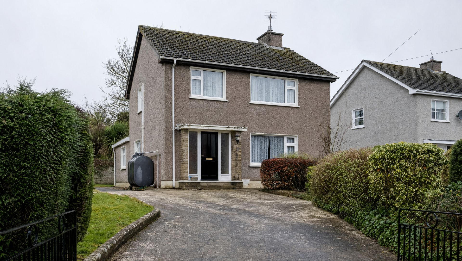 The same house before — grey pebble-dash, old white uPVC windows, a mossy roof and a black oil tank by the door.